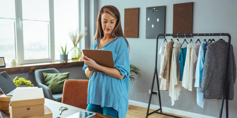 Empreendedora em sua loja de roupas anotando gastos para pesquisar como informar reajuste de preço para o cliente.