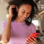 Mulher sorri ao olhar para a tela do celular, em imagem que ilustra artigo sobre comprovante do CNPJ