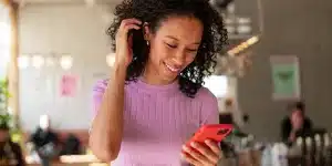 Mulher sorri ao olhar para a tela do celular, em imagem que ilustra artigo sobre comprovante do CNPJ