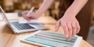 Pessoa faz anotações enquanto checa informações em um tablet, em imagem que ilustra artigo sobre Orçamento contínuo, também chamado de rolling forecast.