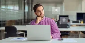 Homem pensa em quanto trabalha em seu laptop. Ao seu redor há ícones financeiros, em fotomontagem que ilustra este artigo sobre boletos Pix como forma de cobrança para empresas.